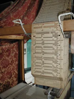 The Jacquard loom: a chain of punched cards above the frame sets the pattern